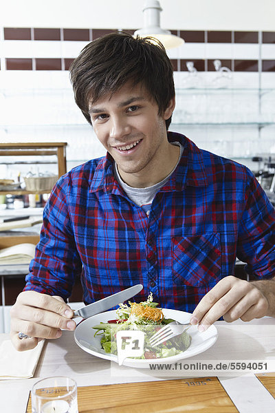 Young man eating salad  smiling  portrait
