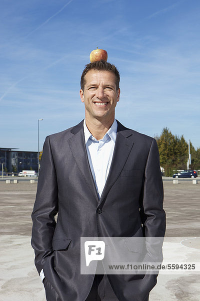 Deutschland  Bayern  München  Geschäftsmann mit Apfel auf dem Kopf  lächelnd  Portrait