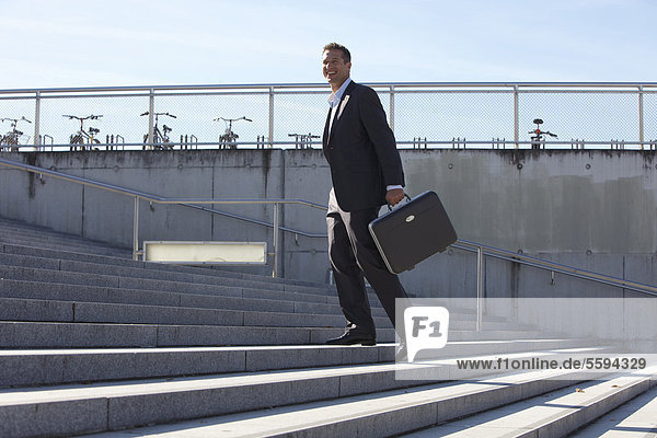 Deutschland  Bayern  München  Geschäftsmann auf der Treppe mit Aktentasche  lächelnd