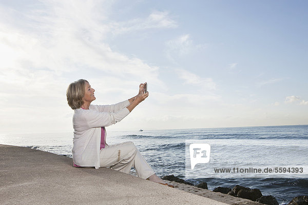 Spanien  Mallorca  Seniorin sitzend und telefonierend am Meer  lächelnd