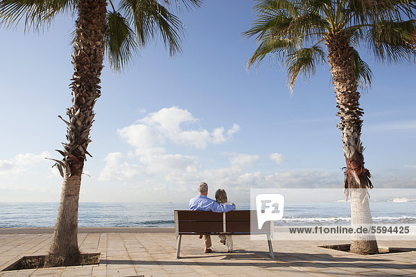 Spanien  Mallorca  Seniorenpaar auf Bank am Meer sitzend