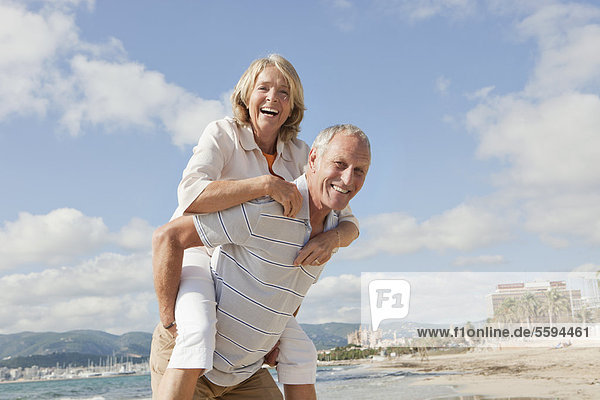 Spanien  Mallorca  Senior Mann  der die Frau am Strand huckepack reitet.