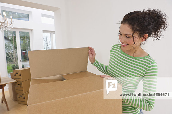 Mittlere erwachsene Frau beim Verpacken von Pappkartons im Haus  lächelnd