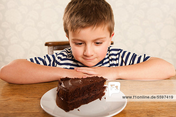 Junge schaut sich ein Stück Schokoladenkuchen an.
