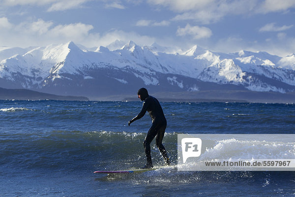 Man surfing along the coastline in Winter with Chilkat Range in the background  Eagle Beach  Southeast Alaska