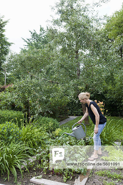 Frau bewässert Pflanzen im Hinterhof