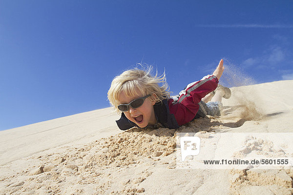 Lächelnder Junge rutscht die Sanddüne hinunter