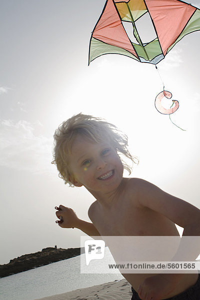 Lächelnder Junge beim Drachenfliegen am Strand