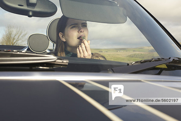 Woman applying lipstick in car mirror