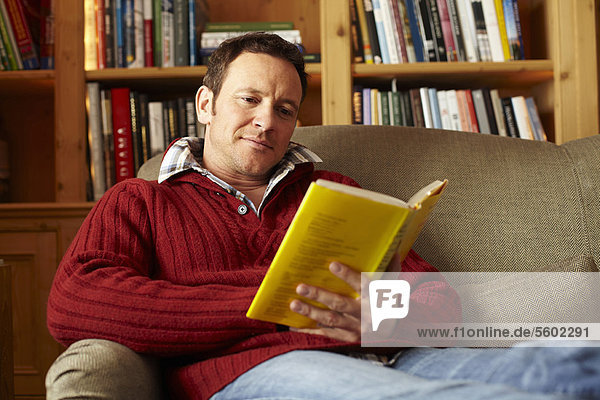 Mann liest Buch auf Sofa