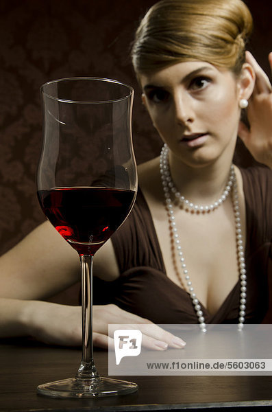 Junge Frau mit Perlenkette und Perlenohring  davor Rotwein im Rotweinglas