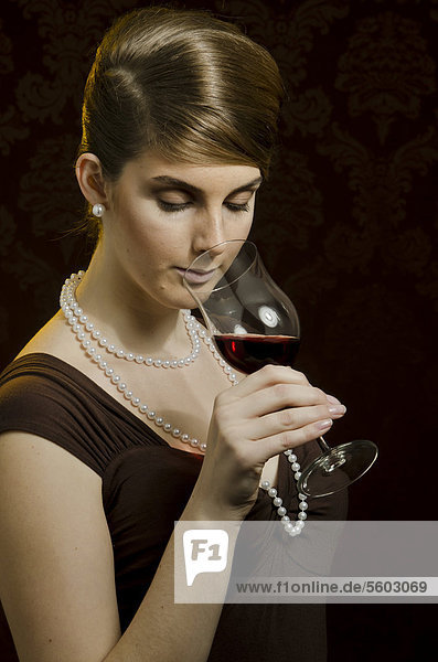Young woman wearing a pearl necklace and pearl earrings  drinking red wine in a wine glass
