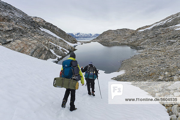 Wanderer mit Rucksäcken auf Schneefeld  See  am Sermilik Fjord  Halbinsel Ammassalik  Ostgrönland  Grönland