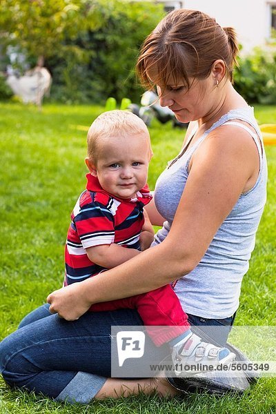 Portrait of young mother with toddler sitting outdoors in the grass