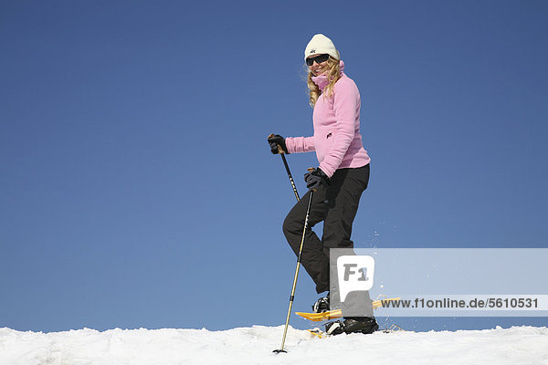 Junge Frau  etwa 25 Jahre  beim Schneeschuhfahren mit Stöcken in der Hand  vor stahlblauem Himmel  Thüringer Wald  Thüringen  Deutschland  Europa