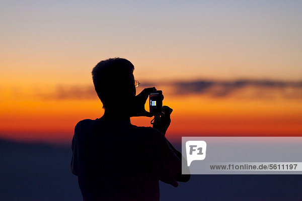 Ein Mann fotografiert mit Handy oder Kompaktkamera  Silhouette im Gegenlicht im Abendrot