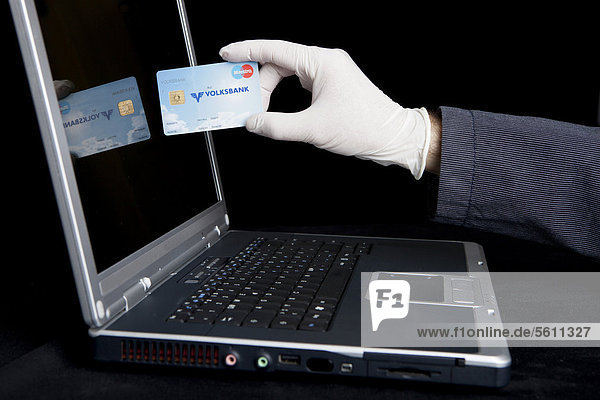 Hacker using a laptop  holding a Eurocard and wearing latex gloves to leave no traces  symbolic image for Internet crime