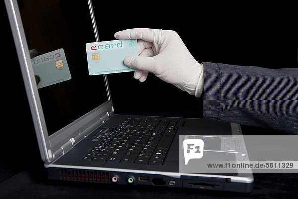 Hacker using a laptop  holding a health insurance card  symbolic image for welfare fraud