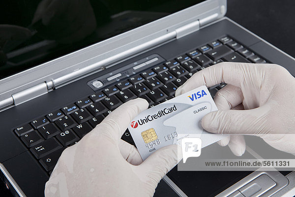 Hacker using a laptop  holding a Visa card and wearing latex gloves to leave no traces  symbolic image for Internet crime