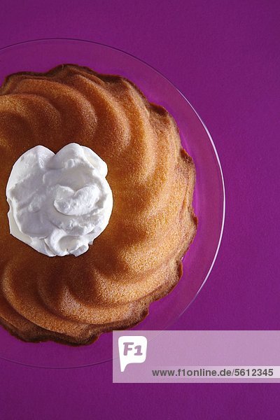 Ring-shaped cake with cream blob on glass plate