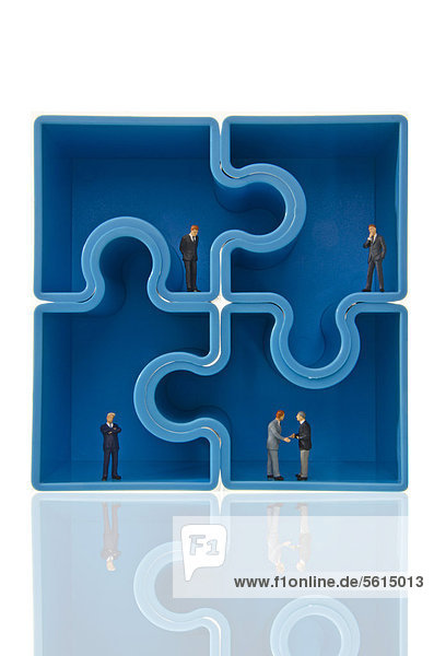 Vier blaue Puzzleteile bilden Quadrat  darin Geschäftsleute  Miniaturfiguren  Symbolbild