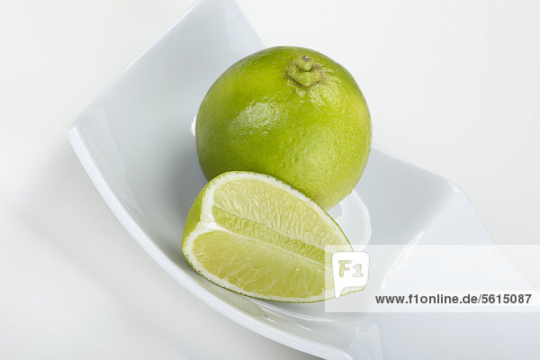 Limetten (Citrus latifolia)  ganz und geschnitten  in einer weißen Schale