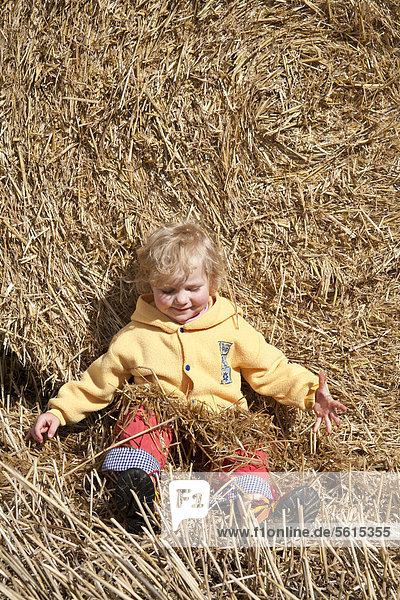 Little girl leaning against a straw bale playing with straw  Saxony  Germany  Europe