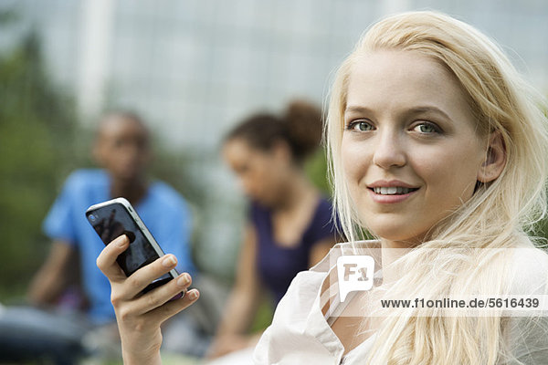 Junge Frau mit Handy  Menschen im Hintergrund  Portrait