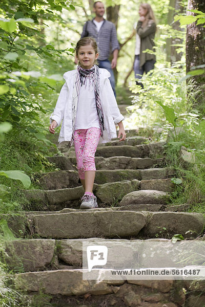 Girl walking down stone steps in woods  parents in background
