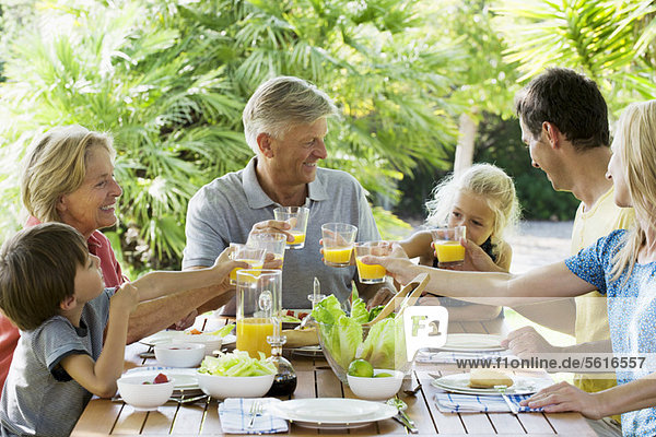 Multi-generation family toasting with orange juice outdoors  portrait