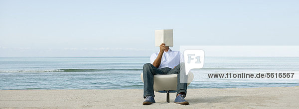 Mann liest Buch am Strand