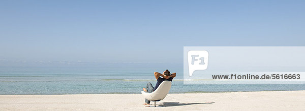 Mann entspannt im Stuhl am Strand  Rückansicht
