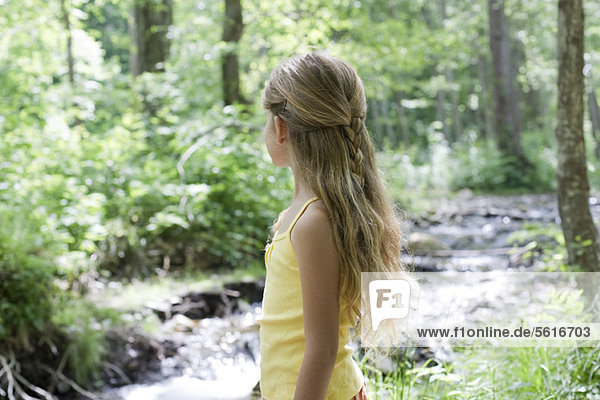 Girl by stream in woods  looking away