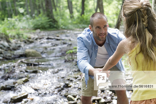 Father helping daughter crossing stream