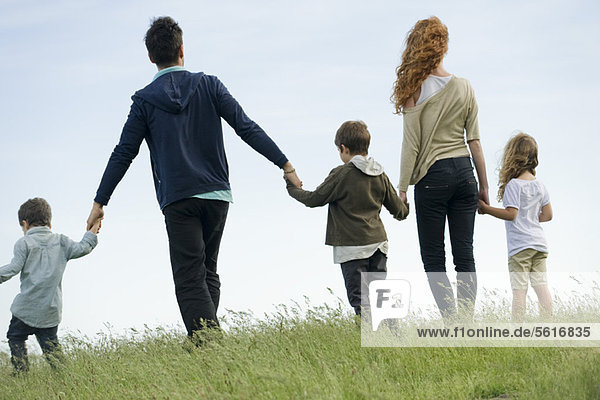 Family walking hand in hand in field  rear view