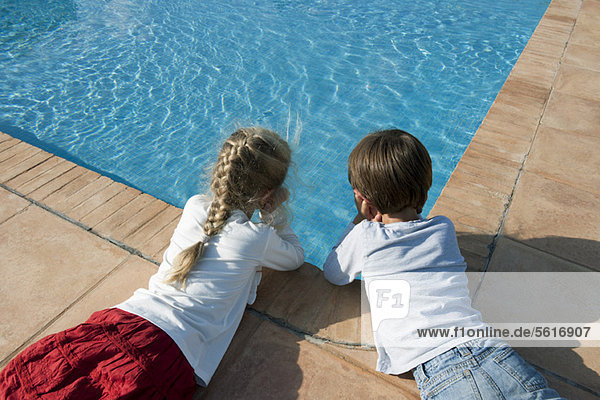Kinder  die neben dem Schwimmbad liegen und das Wasser betrachten