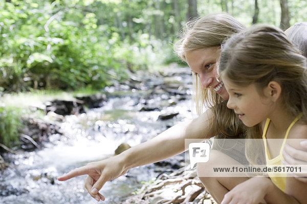 Mother and daughter looking at stream in woods