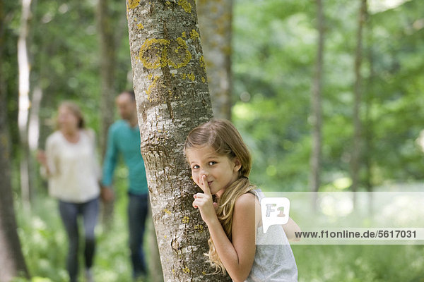 Girl hiding behind tree with finger on lips