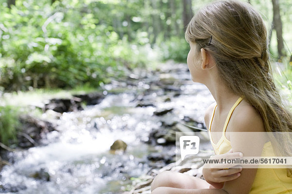 Girl contemplating stream in woods