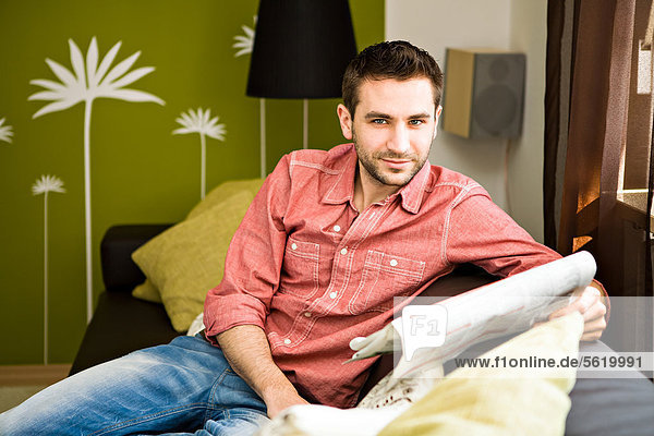 Young man at home  reading a newspaper