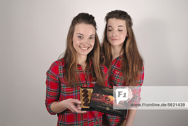 Zwillingsschwestern  die eine hat eine Schachtel Pralinen in der Hand  die andere schaut hinein