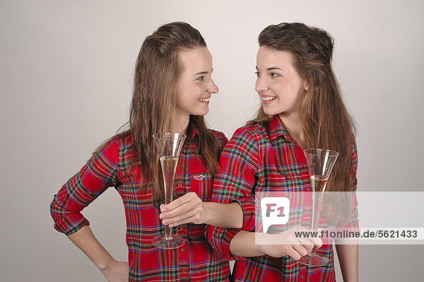 Twin sisters drinking to brotherhood from champagne glasses