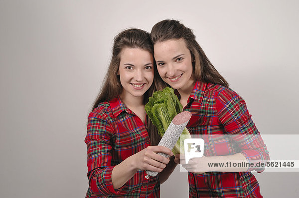 Twin sisters  one holding a salami in her hand  the other holding a head of lettuce