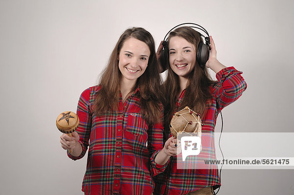 Twin sisters  one playing with rattles  the other listens with headphones