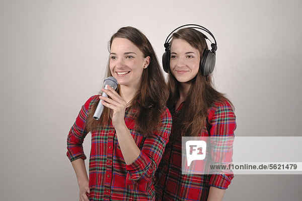 Zwillingsschwestern  die eine singt in ein Mikrofon  die andere hört mit Kopfhörern
