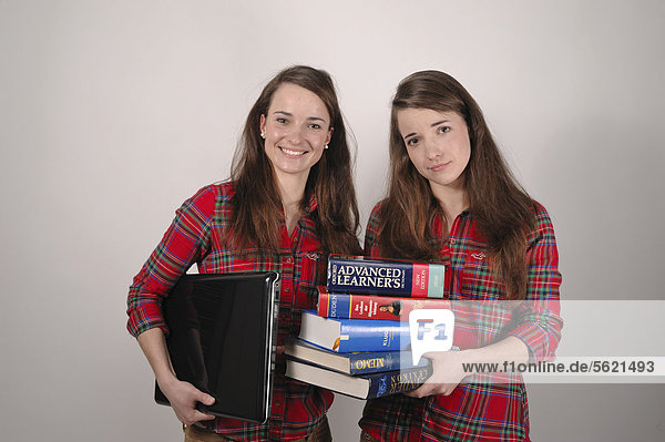 Zwillingsschwestern  die eine mit einem Laptop  die andere mit einem Stapel Bücher