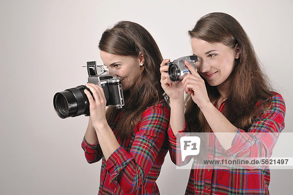 Twin sisters holding cameras  one holding a Pentacon Six medium format analogue camera  the other holding a digital camera