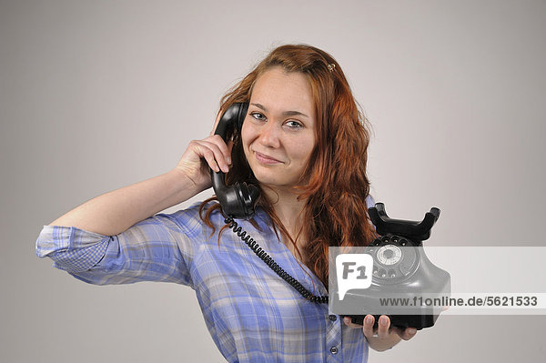 Junge Frau mit roten Haaren telefoniert mit einem alten Wählscheibentelefon