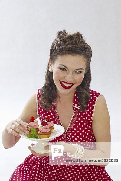 Mädchen im Retro-Look hält Teller mit Erdbeermuffins