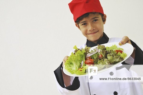 Junge als Koch hält einen Salatteller